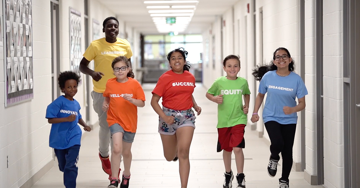 six student walking in school hallway wearing coloured T-shirts reflecting the DDSB's strategic priorities