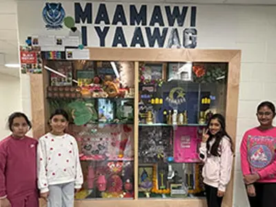 Maamawi Iyaawag students standing in front of display case.